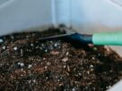 Composteira doméstica de plástico com três camadas aberta mostrando camadas de resíduos orgânicos e terra