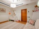 Quarto de bebê neutro com berço de madeira clara, móbile minimalista, paredes off-white e iluminação suave