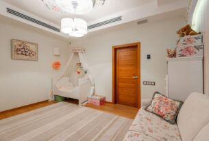 Quarto de bebê neutro com berço de madeira clara, móbile minimalista, paredes off-white e iluminação suave