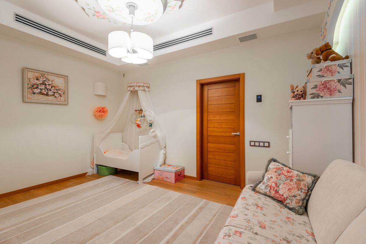 Quarto de bebê neutro com berço de madeira clara, móbile minimalista, paredes off-white e iluminação suave